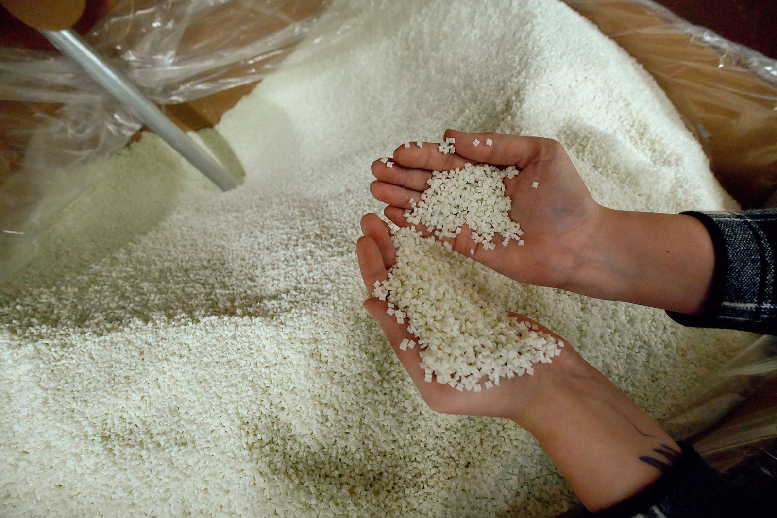 Hands cupping white resin pellets over a bulk container at Wise Plastics