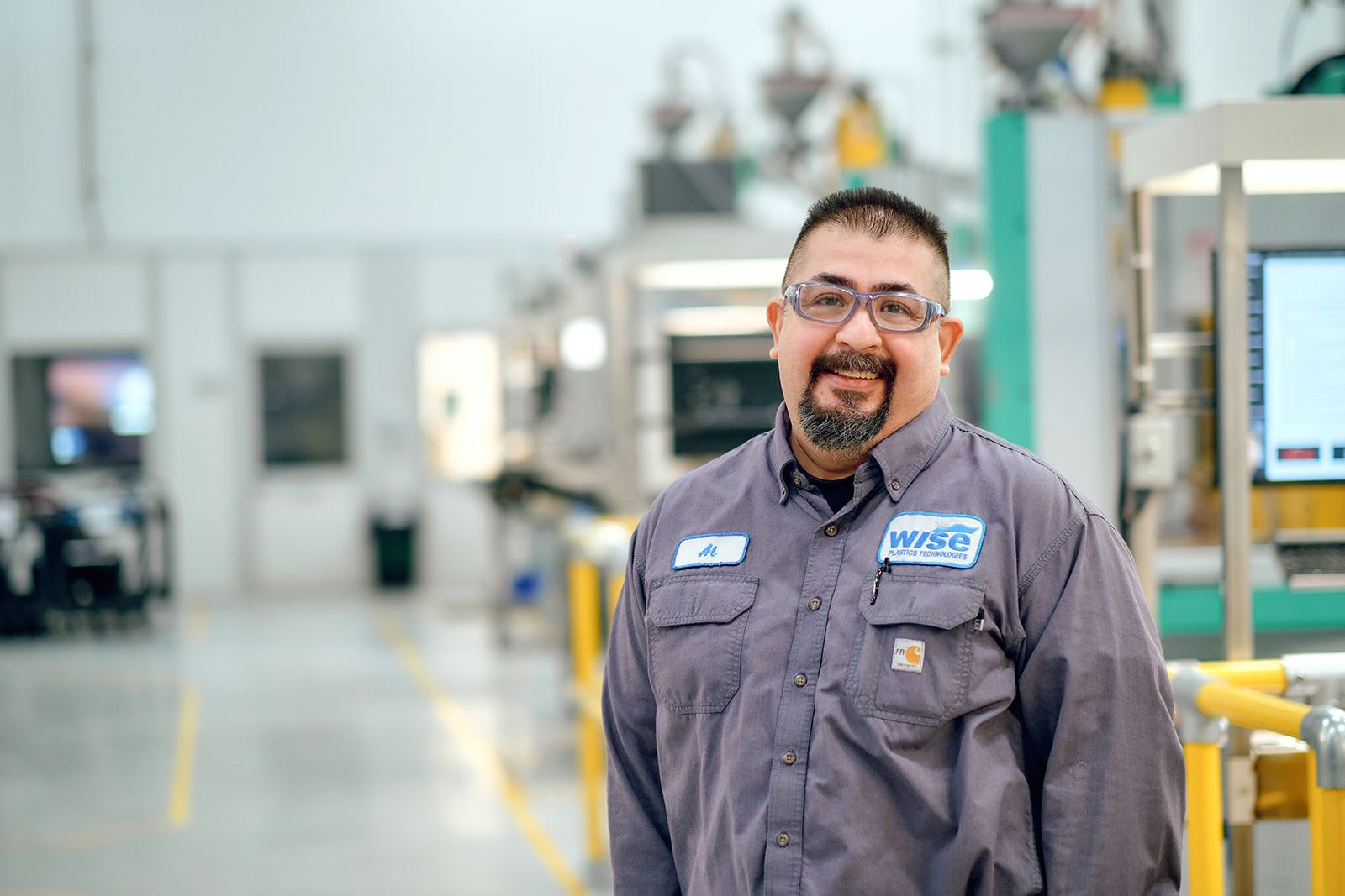 Smiling Wise Plastics maintenance technician standing in an aisle of injection molding presses at the St. Charles Illinois facility