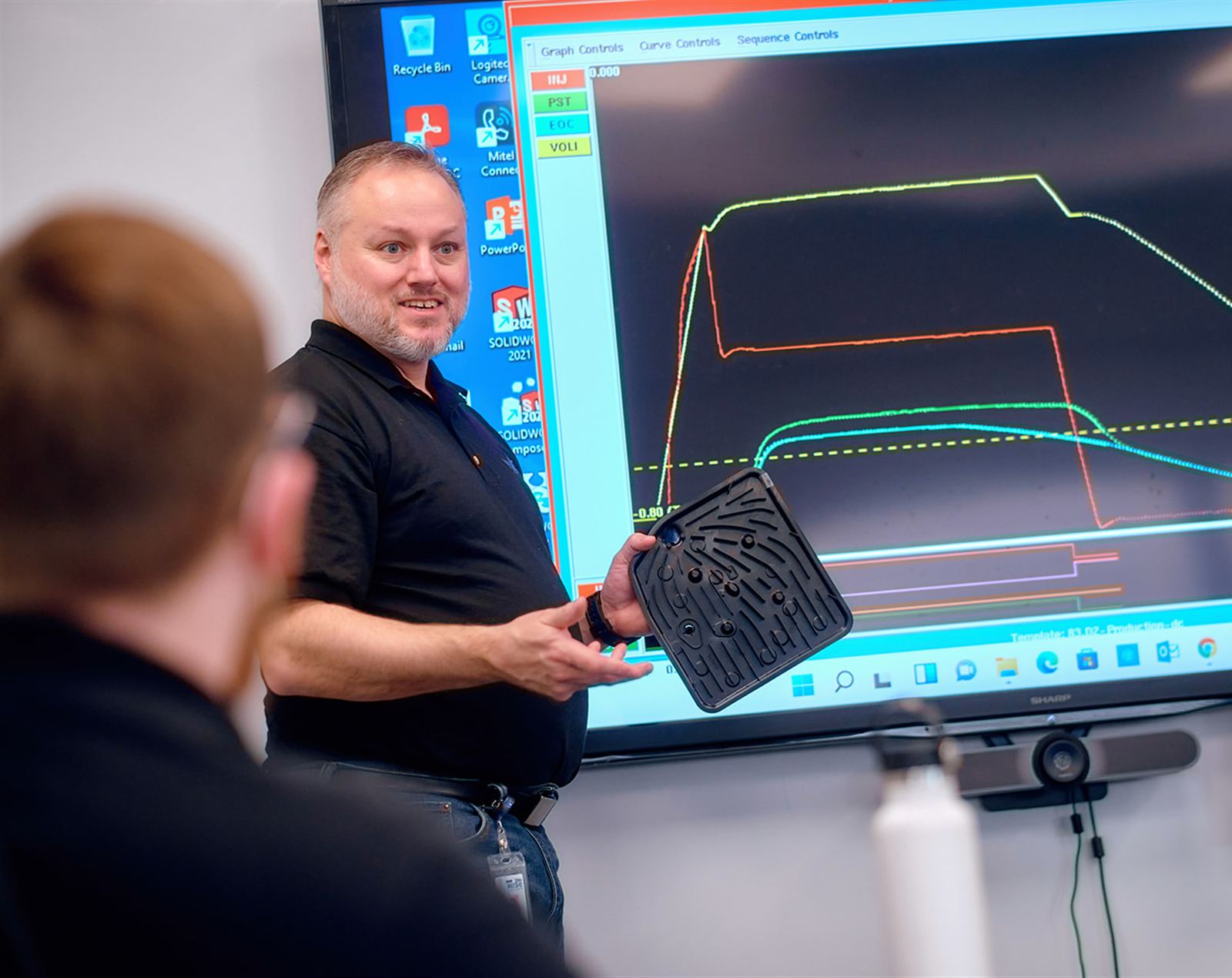 Wise Plastics process engineer holding a molded part while explaining an injection cycle graph
