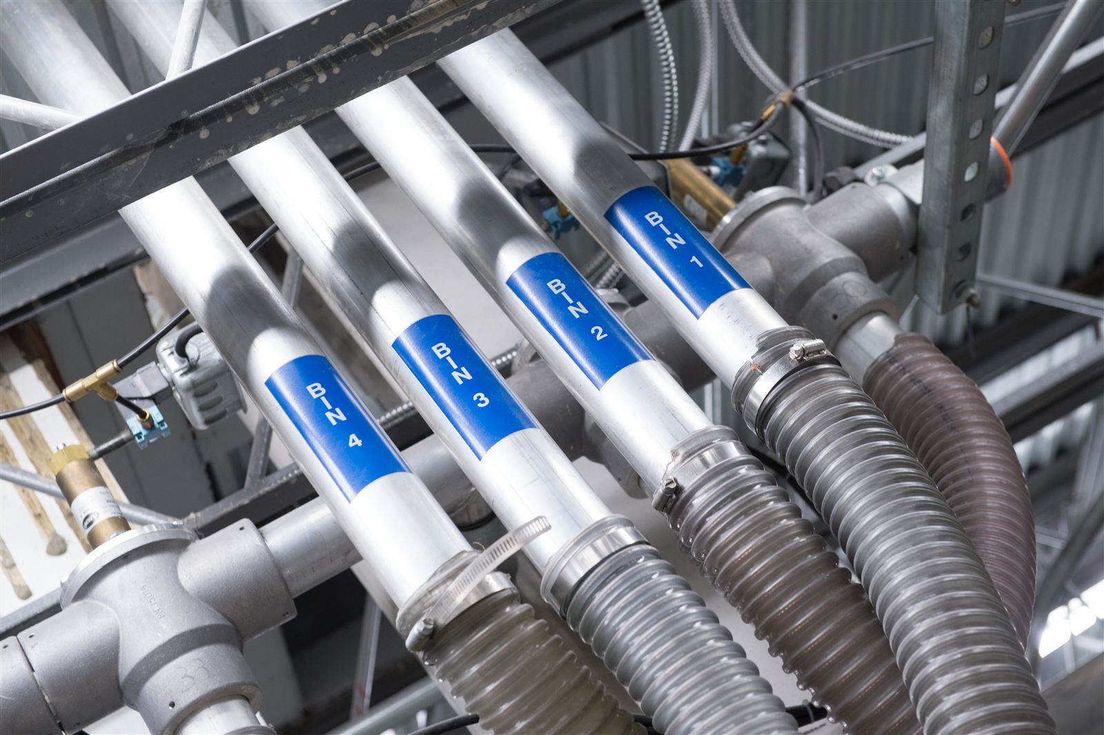 Labeled central resin feed lines carrying dried material from bulk storage to the molding presses at Wise Plastics