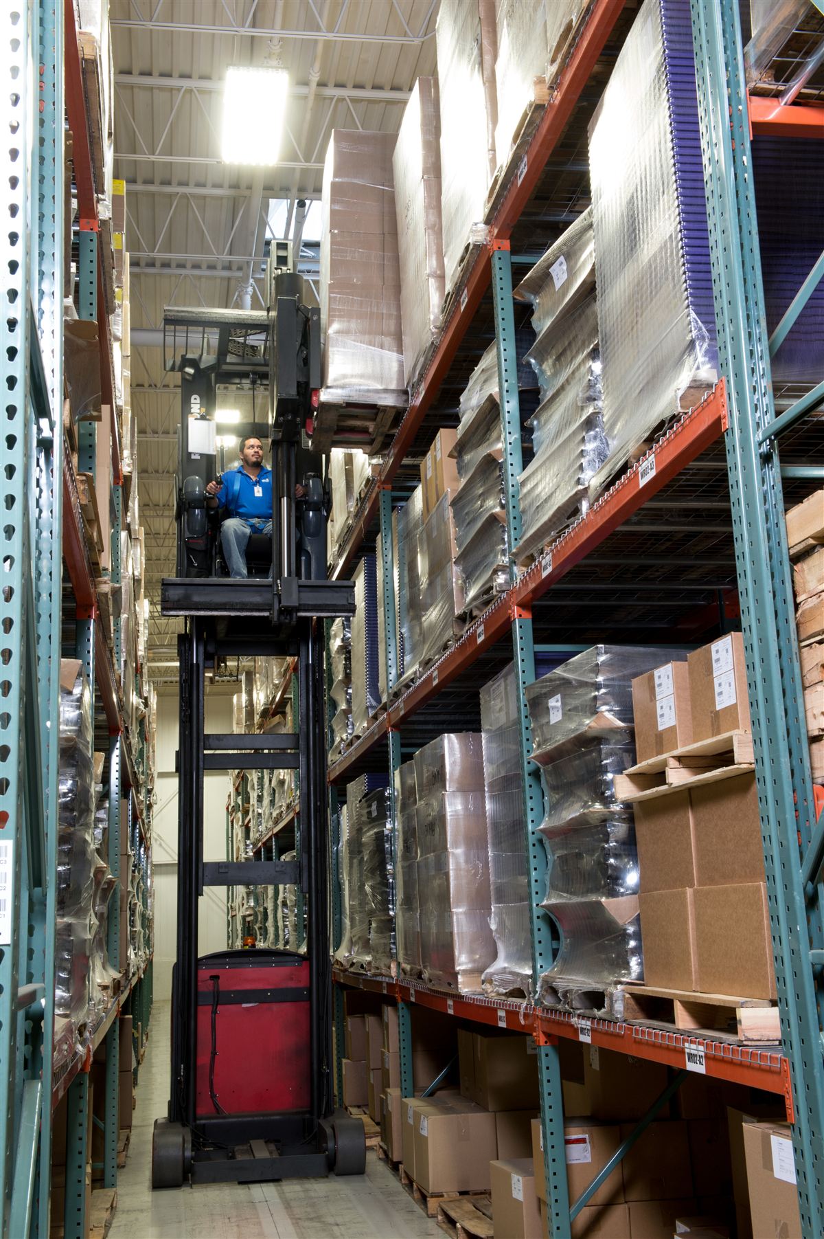 Order picker raised in a high-bay racking aisle stocked with wrapped finished goods at the Wise Plastics warehouse